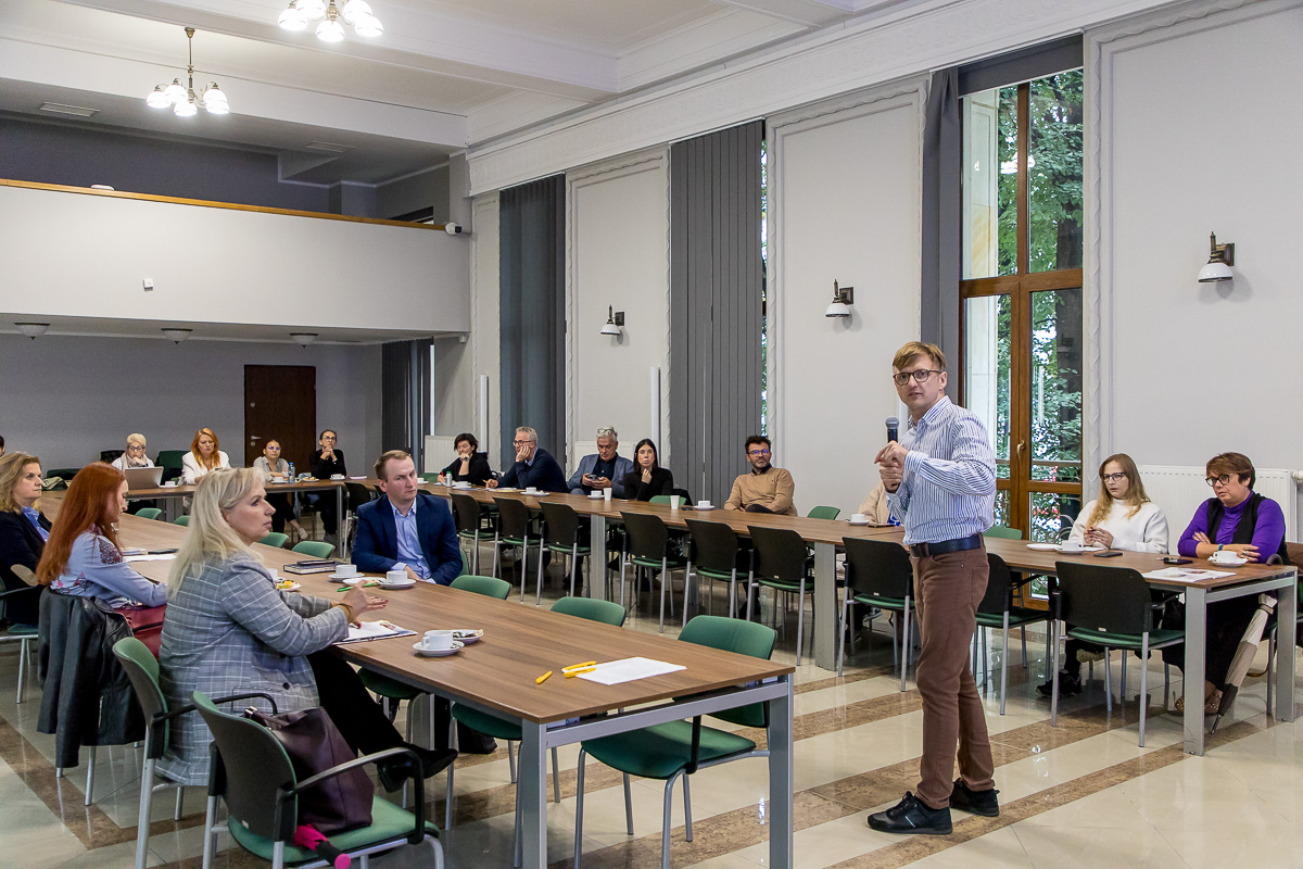 Dorosłe osoby rozmawiające przy stole, prelegent podczas wykładu.