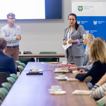 Dorosłe osoby rozmawiające przy stole, prelegent podczas wykładu.