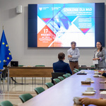 Dorosłe osoby rozmawiające przy stole, prelegent podczas wykładu.