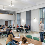 pan Tomasz Pawłowski stoi  i przemawia do grupy uczestników szkolenia siedzących przy stołach