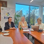 Dorota Konieczny-Simela, Beata Twardowska oraz Dorota Tobiszowska siedzą przy drewnianym stole konferencyjnym w jasnej sali z dużym oknem, przez które widać drzewa. W tle baner z logo RDPP 